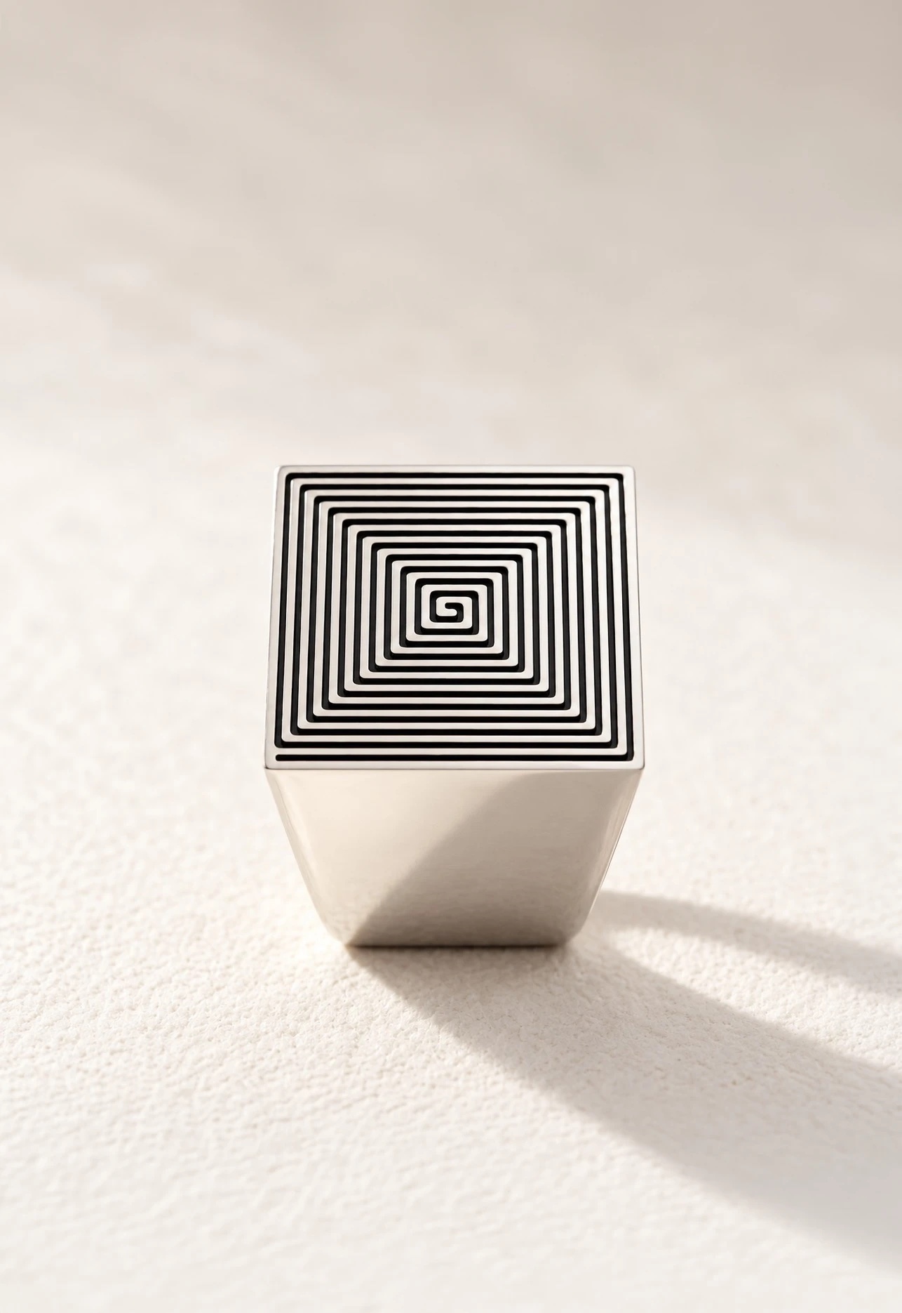 Signet 01 in polished sterling silver standing face up on a pale surface, the twelve-turn labyrinth on its square face